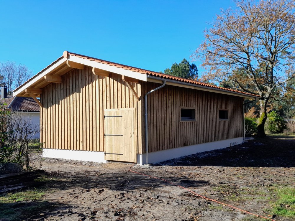 Grange en bois d'inspiration landaise traditionnelle avec chemin d'accès en gravier et portail bois